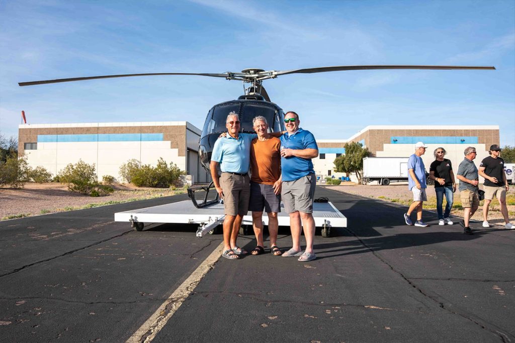 three men standing in front of a helicopter